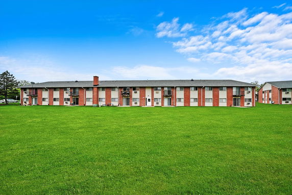 Front view of a long, two-story apartment building with a grass lawn.