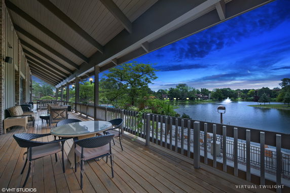 Covered outdoor porch with seating overlooking a lake and trees.