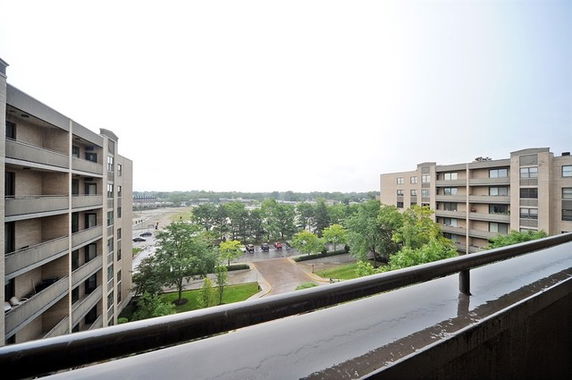 View from a balcony overlooking two apartment buildings and a parking area with trees.