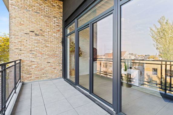 Open rooftop balcony with large sliding glass doors and brick wall.