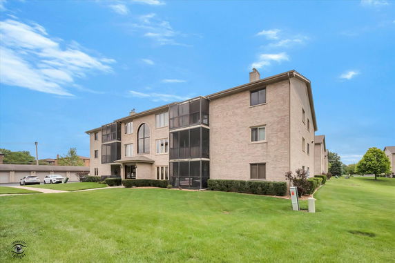 Front view of a multi-story residential building with balconies and a landscaped lawn.