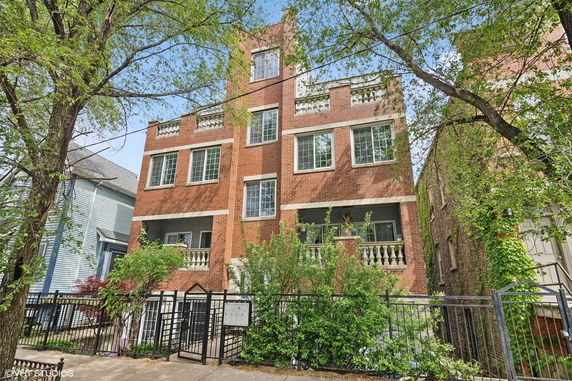 Front view of a multi-story brick building with balconies and a gated entrance.