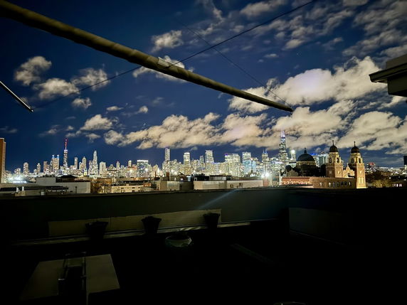 Panoramic view of a city skyline at night with illuminated buildings and clouds.