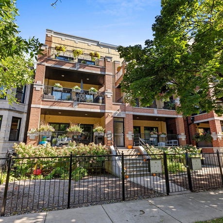 Front view of a multi-story brick apartment building with balconies and landscaping.