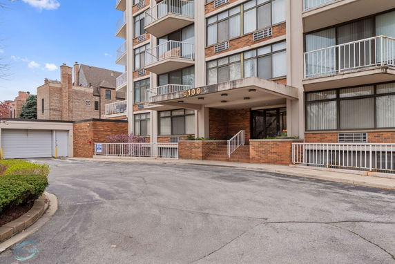 Front view of a multi-story apartment building with balconies and a driveway.