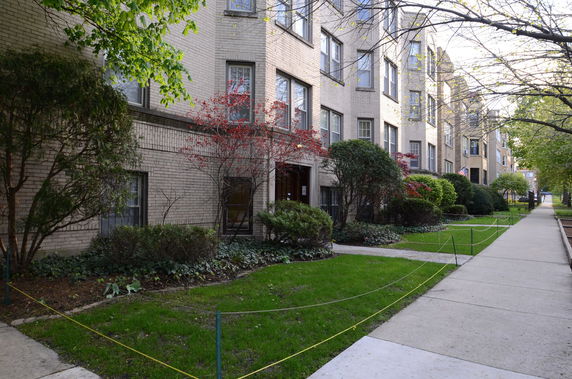 Front view of a multi-story brick building along a sidewalk with landscaping.