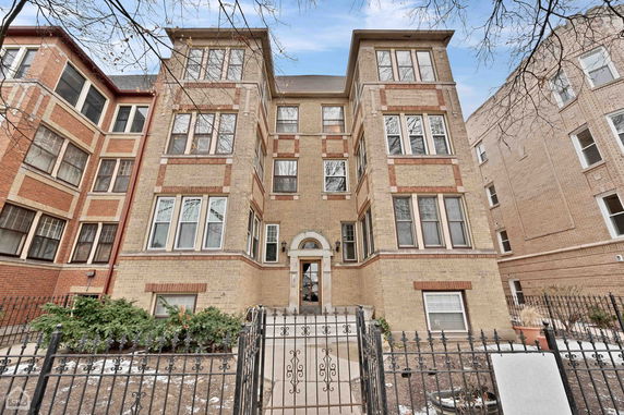 Front view of a multi-story brick building with large windows and a gated entrance.