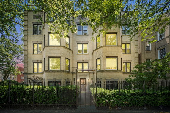 Front view of a multi-story brick apartment building with large windows and gated entrance.