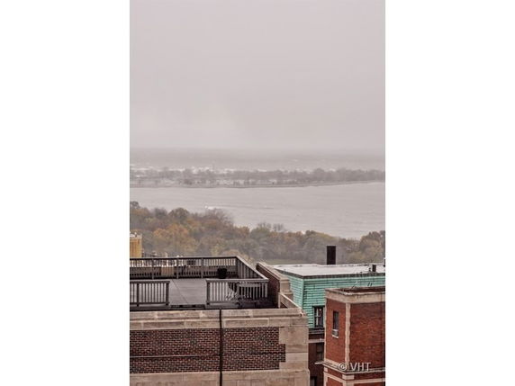 Rooftop of a building with railing, overlooking water and trees in the distance.