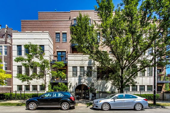 Front view of a multi-story residential building with trees and parked cars.