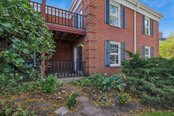 Front view of a two-story brick house with balcony and blue shutters.