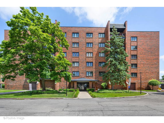 Front view of a six-story brick apartment building with trees and a driveway.
