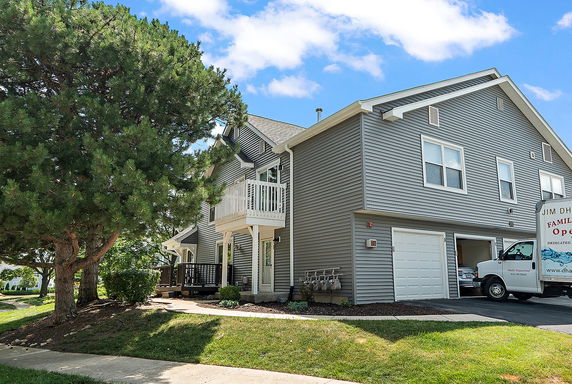 Front view of a two-story house with gray siding and a small balcony over the entrance.