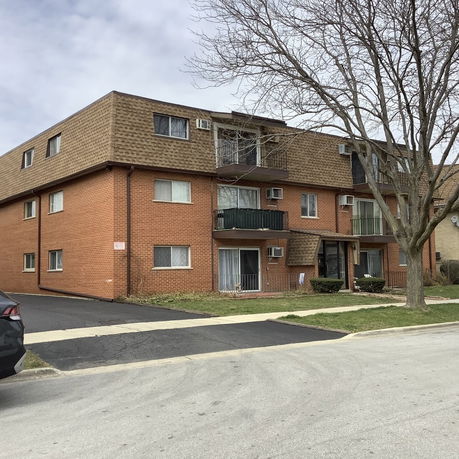 Front view of a three-story brick apartment building with multiple balconies.