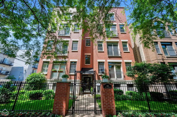 Front view of a multi-story brick apartment building with a gated entrance.