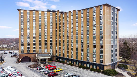 Front view of a multi-story apartment building with numerous windows and a parking area in front.