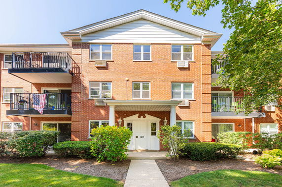 Front view of a multi-story brick apartment building with balconies and white entrance door.