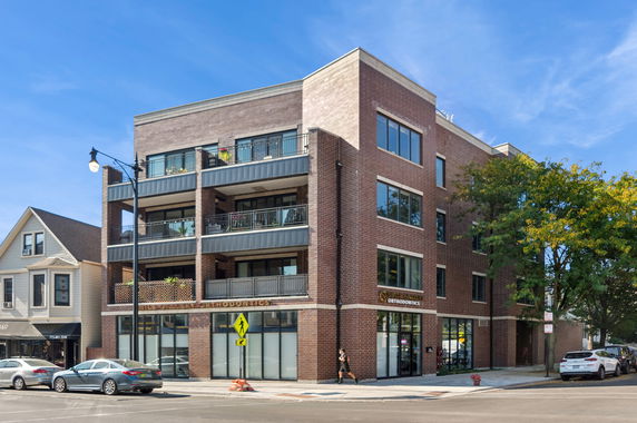 Front view of a multi-story brick building with balconies and large windows on a street corner.
