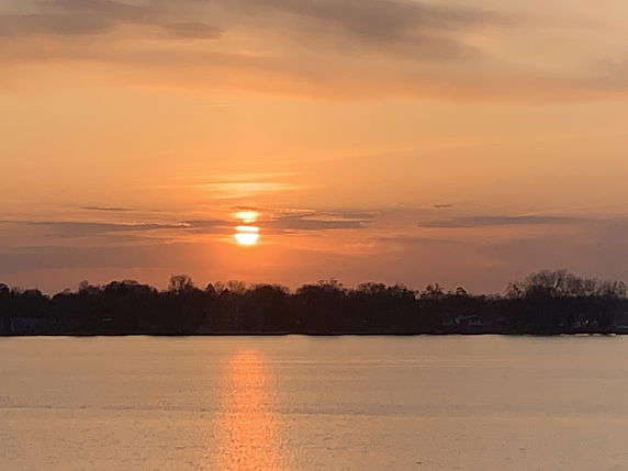 Panoramic view of a sunset over a body of water with a silhouette of trees in the background.
