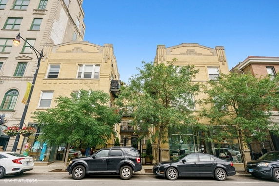 Front view of a multi-story building with trees and parked cars in front.