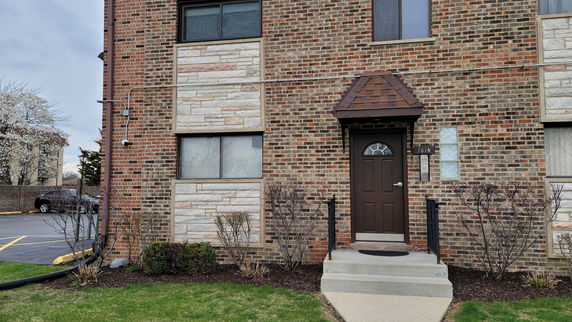 Front view of a brick house entrance with brown door and steps.