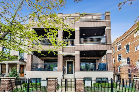 Front view of a multi-story brick building with balconies and a gated entrance.