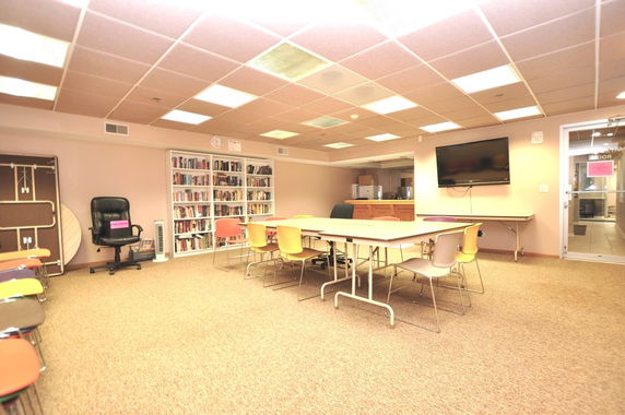 Indoor room with tables, chairs, bookshelves, and a television.
