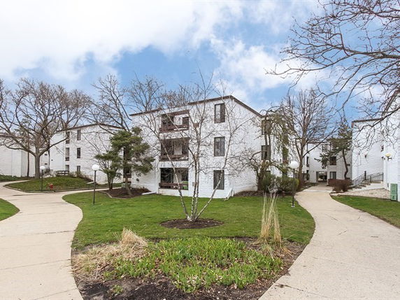 Front view of a multi-story apartment building with pathways and grassy area.