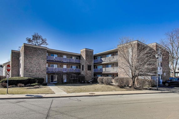 Front view of a three-story brick apartment building with balconies.