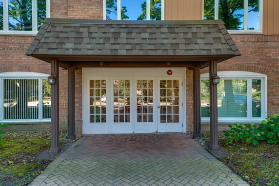 Front view of a building entrance with a shingled awning and glass double doors.