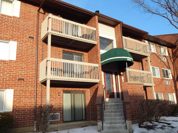 Front view of a multi-story brick building with balconies and a green awning over the entrance.