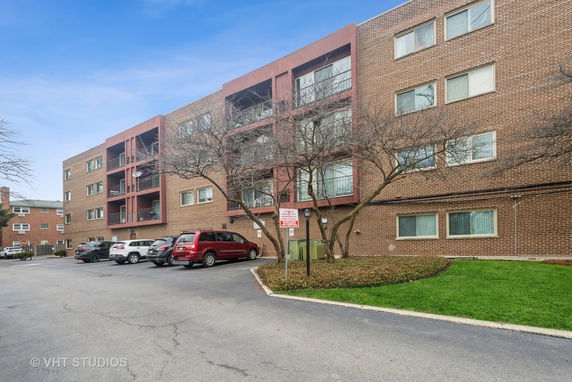 Front view of a multi-story brick apartment building with parking area in front.