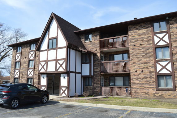 Front view of a multi-story brick apartment building with wooden accents and balconies.