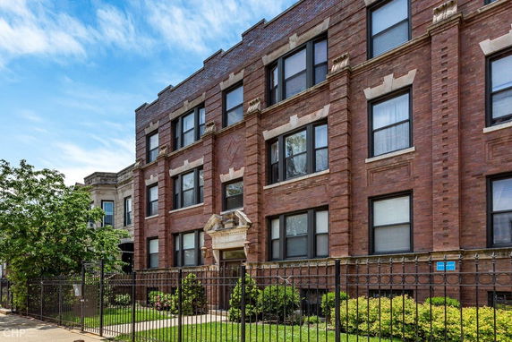 Front view of a three-story brick building with large windows and a gated entrance.