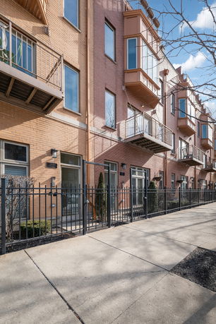 Front view of a multi-story brick building with several balconies and a metal fence.
