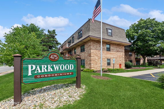 Front view of a brick condominium building with an American flag and signage for 'Parkwood Condominiums'.