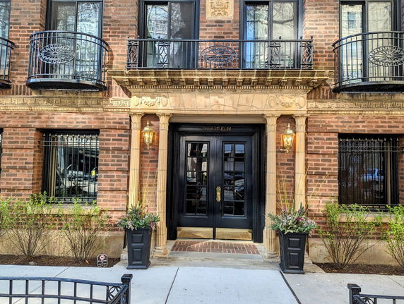 Front view of a brick building with decorative balcony railings and a central entrance.