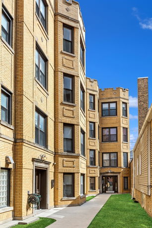 Front view of a multi-story brick apartment building with large windows and a central pathway.
