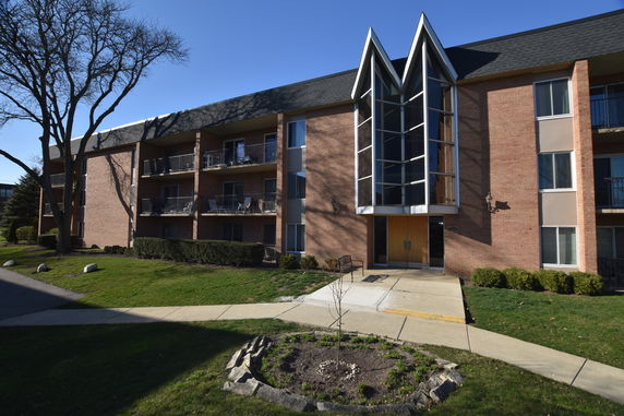 Front view of a three-story building with balconies and a distinctive glass entrance.