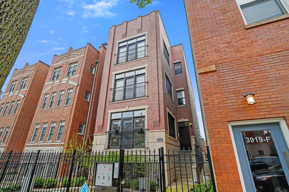 Front view of a multi-story brick building with balconies and a gated entrance.