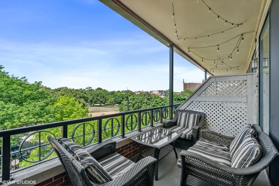 View from balcony with outdoor seating area overlooking trees and nearby buildings.