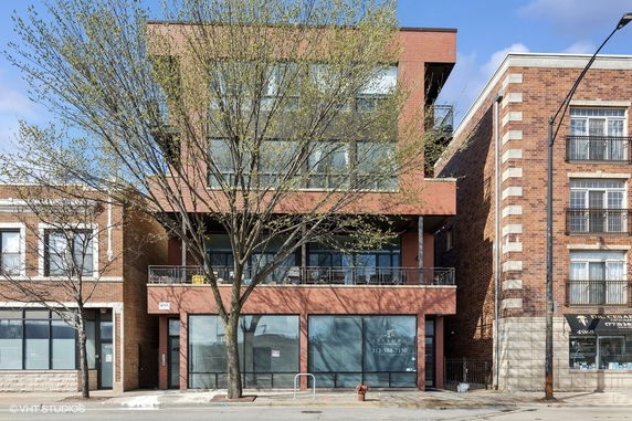 Front view of a modern three-story building with large glass windows and a brick facade.