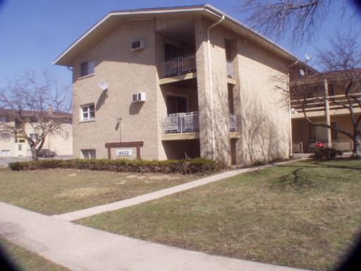 Front view of a three-story brick building with balconies and a sloped roof.
