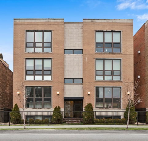 Front view of a three-story brick apartment building with large windows and a central entrance.