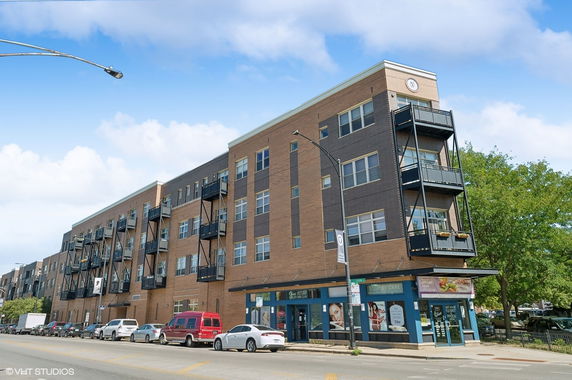 Front view of a multi-story building with balconies and commercial units on the ground floor.