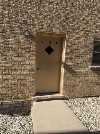 Front view of a building showing a door with a diamond-shaped window and adjacent wall with a light fixture.