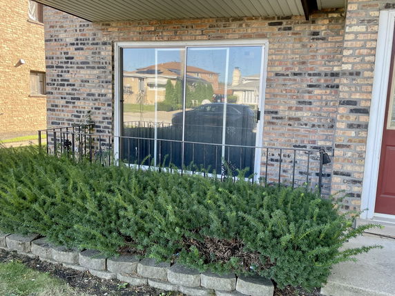 Front view of a brick house with a large window and a small garden.