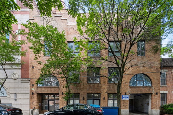 Front view of a multi-story brick building with large arched windows and car parked in front.