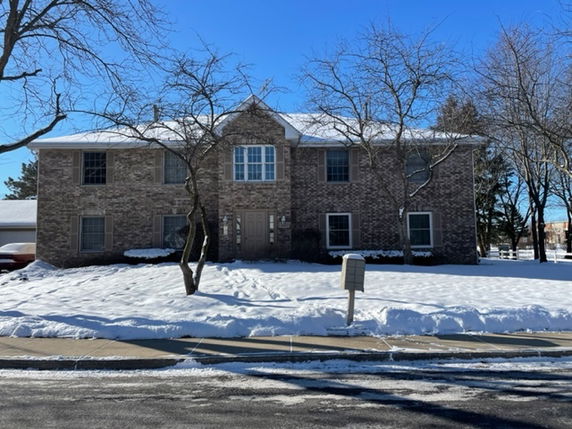 Front view of a two-story brick house with snow-covered surroundings.