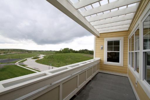 A balcony area with a white pergola, overlooking a grassy landscape.